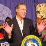 Man speaking at podium with smiling audience behind.
