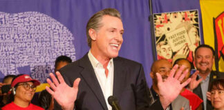Man speaking at podium with smiling audience behind.