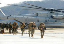 Marines walking away from helicopter on airstrip.