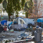 FAKE Homeless Encampment Sparks LA Race Showdown! Homeless encampment with tents and trash in urban area.
