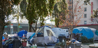 Homeless encampment with tents and trash in urban area.