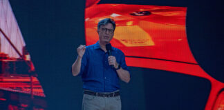 Stephen Colbert speaking on stage with a vibrant backdrop