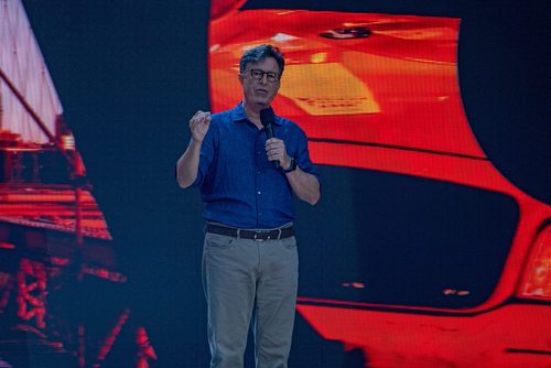 Stephen Colbert speaking on stage with a vibrant backdrop