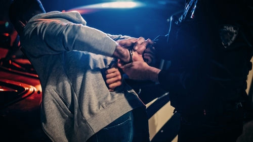 shutterstock_2232056691.jpg Person being handcuffed by police officer at night.