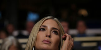 A woman with long blonde hair and earrings looking thoughtfully during an event