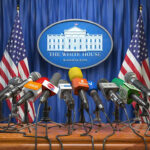 White House podium with multiple microphones and flags.