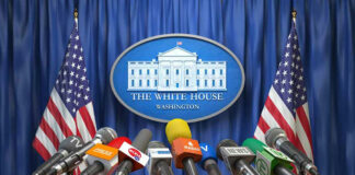 White House podium with multiple microphones and flags.
