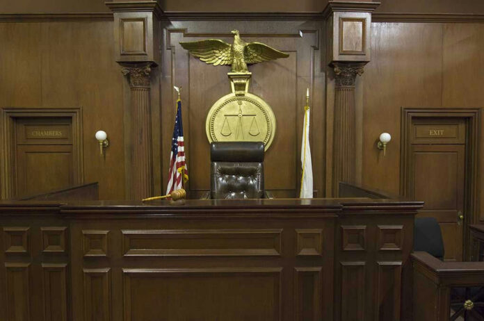 121502698-1 Judges bench in an empty courtroom, scales emblem above.