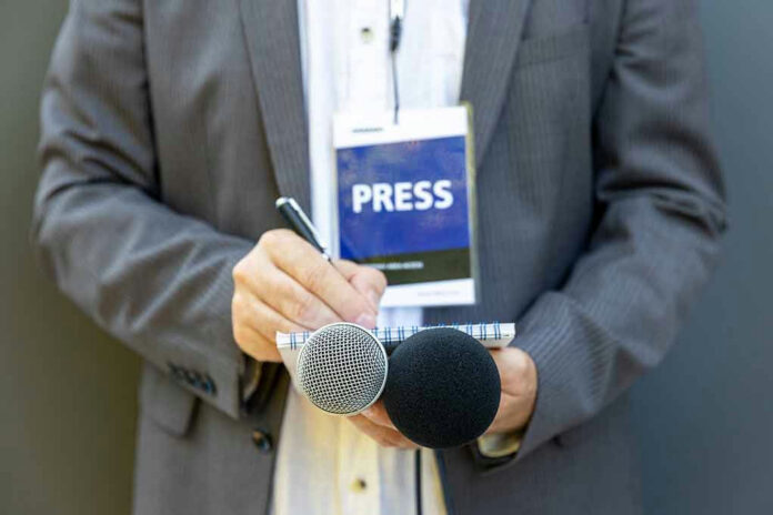 1808083621 Press member holding microphones and taking notes.