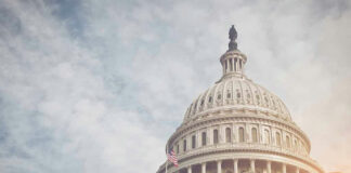 US Capitol dome with American flag and cloudy sky.