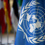 United Nations flag with various country flags in background.