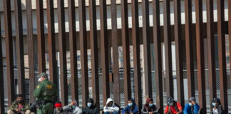 Border patrol agent with group of seated immigrants.