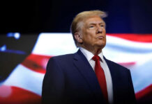 Peace Through Strength Or Dangerous Escalation? donald trump in suit with red tie American flag backdrop