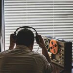 SECRET SPY LAW Quietly Lives On Person wearing headphones listening to a reel-to-reel tape recorder
