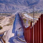 Traffickers STOPPED – HEAVILY Smuggling Corridor FINALLY CLOSED! Border wall stretching through desert landscape with mountains.
