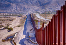 Border wall stretching through desert landscape with mountains.