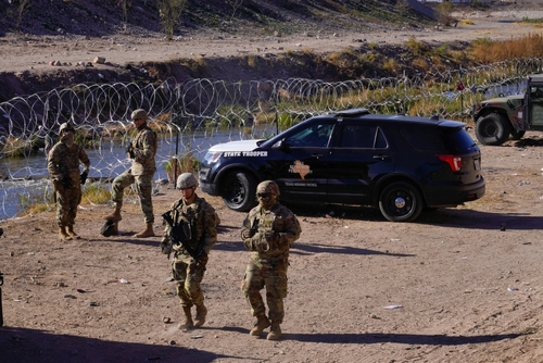 Military personnel and law enforcement officers near a border area with vehicles and barbed wire