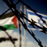 Barbed wire in the foreground with Palestinian and Israeli flags in the background