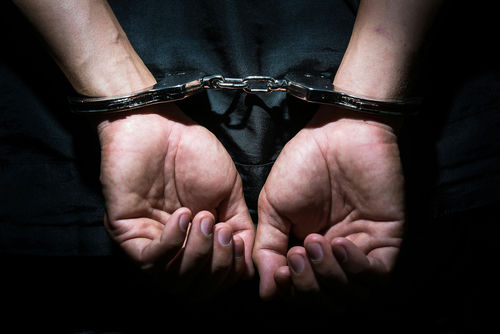 shutterstock_313661888 Two hands in handcuffs behind back in dim light.