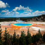 Grand Prismatic Spring with trees and mountains in background.