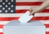 Hand casting ballot into box before U.S. flag