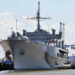 Large naval ship docked at an industrial port.