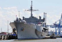 How One Warship Became A Budget Disaster Large naval ship docked at an industrial port.