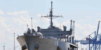 Large naval ship docked at an industrial port.