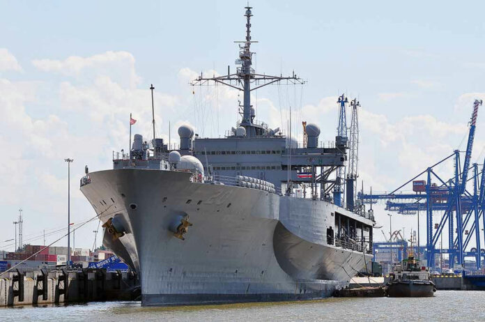 Large naval ship docked at an industrial port.