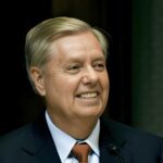 Aortic Tear Suspected — Graham Mystery Deepens Smiling middle-aged man in a suit speaking at a podium