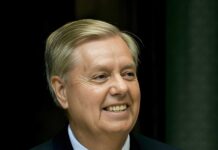 Aortic Tear Suspected — Graham Mystery Deepens Smiling middle-aged man in a suit speaking at a podium