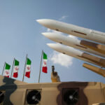 Missiles Survive, Bill Soars — What Now? Missiles on launchers beside Iranian flags.