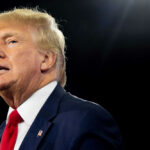 Trump’s Crypto Empire Hits Stunning Milestone Man in suit and red tie speaking on stage