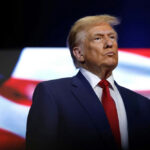 Godless Threat? Trump Warns Of Communists donald trump in suit with red tie American flag backdrop