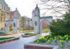 Stone archway entrance on a university campus with blooming yellow flowers