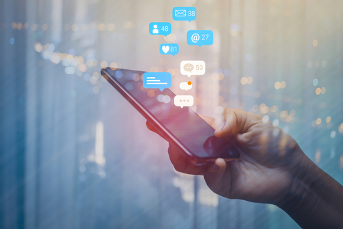 Person,Using,A,Social,Media,Marketing,Concept,On,Mobile,Phone A hand holding a smartphone with social media notifications displayed above it