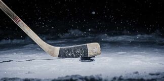 Hockey stick poised over a puck on snowy ice