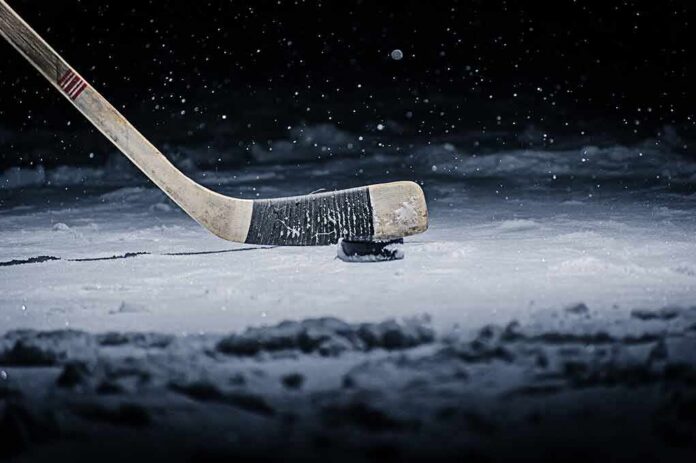 shutterstock_542118652 Hockey stick poised over a puck on snowy ice