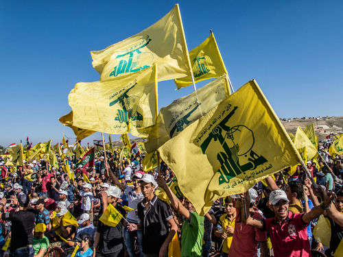 shutterstock_589204028 People waving Hezbollah flags at a large outdoor gathering.