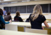 Students seated in a classroom listening to a teacher at the chalkboard