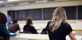 Students seated in a classroom listening to a teacher at the chalkboard