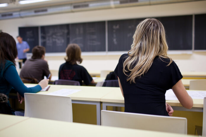 Students seated in a classroom listening to a teacher at the chalkboard