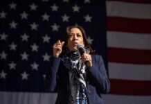 woman speaking into a microphone in front of a large American flag
