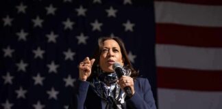 woman speaking into a microphone in front of a large American flag