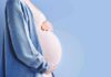 Pregnant person holding belly in blue cardigan