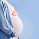 Pregnancy Risk Texts Rock Fauci Narrative Pregnant person holding belly in blue cardigan