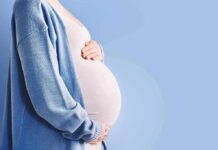 Pregnant person holding belly in blue cardigan