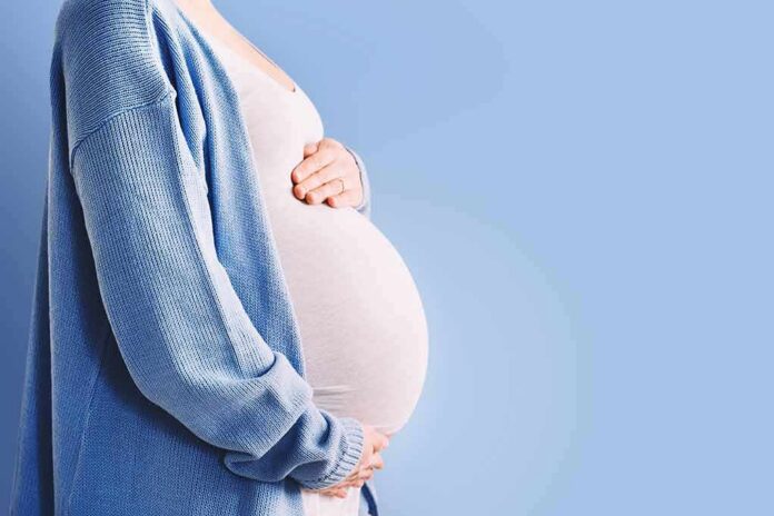 shutterstock_1902288775 Pregnant person holding belly in blue cardigan