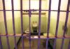 Interior of a prison cell with a toilet, sink, and metal bars
