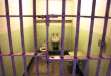 Interior of a prison cell with a toilet, sink, and metal bars
